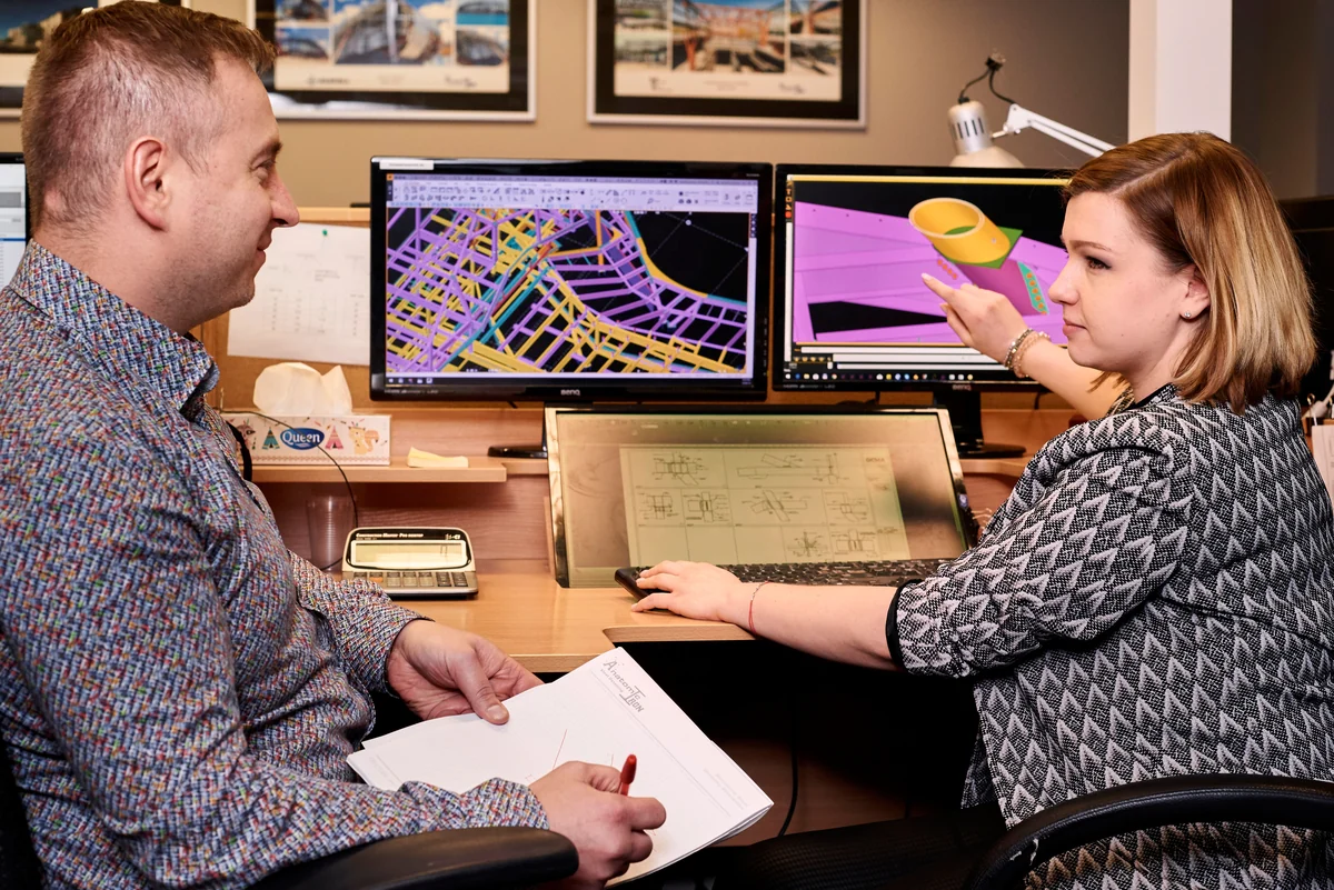 Colleagues discussing steel models and drawings at a workstation
